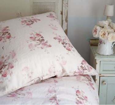 Pink duvet cover with pink flowers next to a sea green nightstand with flowers on it