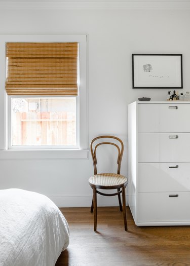 White dresser, wood floors, chair, bamboo blind.