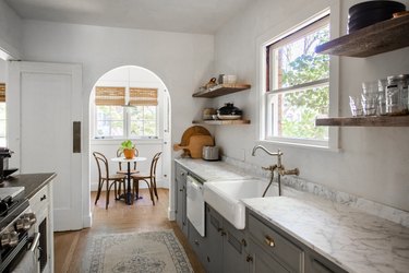 Minimalist kitchen with gray cabinets, wood shelves, farmhouse sink, and granite or marble counters.