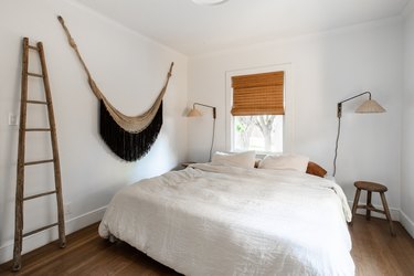 Bedroom with wall hanging, wood ladder, bamboo blinds.
