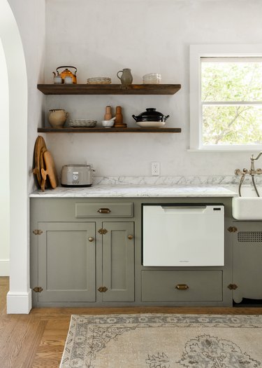 Gray kitchen cabinets, apron sink, open shelves, marble counter.