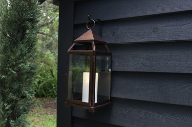 Bronze lantern hanging on black shed with candle inside