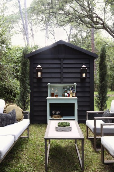 Black painted shed with lanterns serving as cocktail lounge area outside