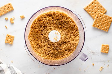 Mixing graham cracker crumbs and butter in a food processor