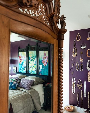 A dark brown armoire with a mirror reflecting a plum walled room and bed.