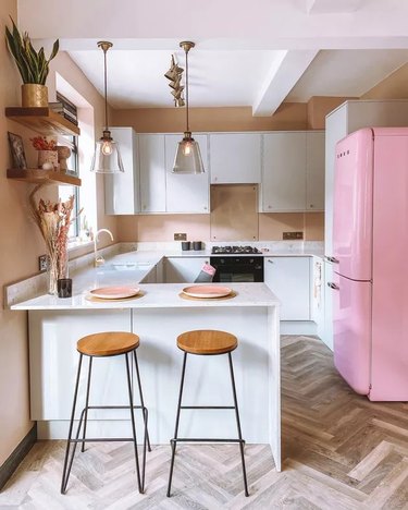 Whimsical pink retro refrigerator in a kitchen with white cabinetry and chevron wooden floors
