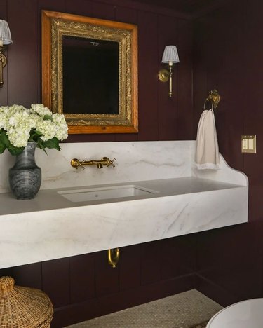 A bathroom vanity, with moody dark plum walls and a large marble sink.