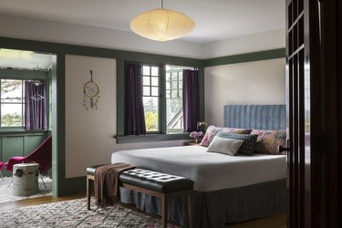 A bedroom with forest green accents, plum curtains, and a white bed.