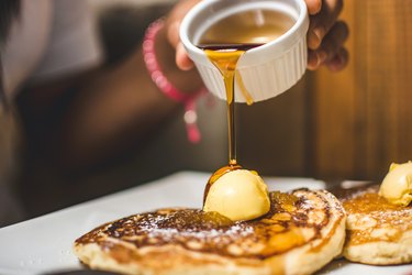 Hand pouring maple syrup on top of pancakes