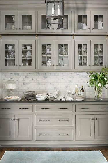 Light gray butler pantry features glass front cabinets with black hardware and black granite countertops