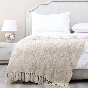 Beige cable knit blanket on a bed with white pillows and comforter