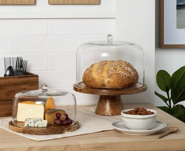 Baked goods and cheese under cake plates on a table with a bowl of nuts