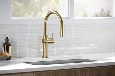 A gold faucet in a kitchen with a glass tile backsplash
