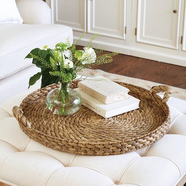 Seagrass tray accessorized with flowers and books on a white ottoman