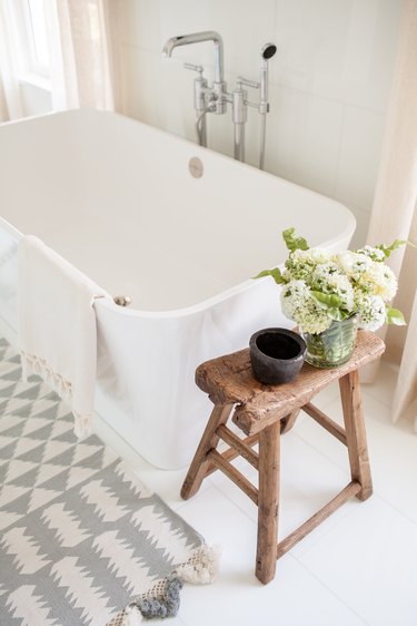 A standalone bathtub with a rustic wood stool.