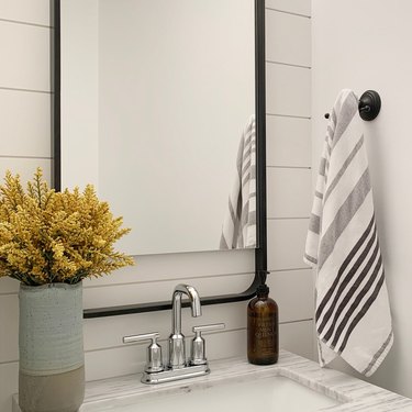Closeup of a bathroom vanity with white walls, a mirror, and a vase of yellow dried florals.