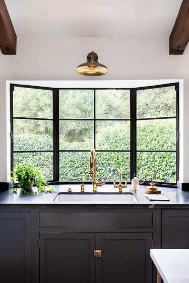ay window in a transitional kitchen features black panels above black leathered countertops and a kitchen sink