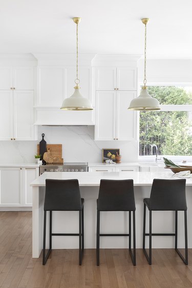 A white kitchen with an island and three dark leather bar stools.