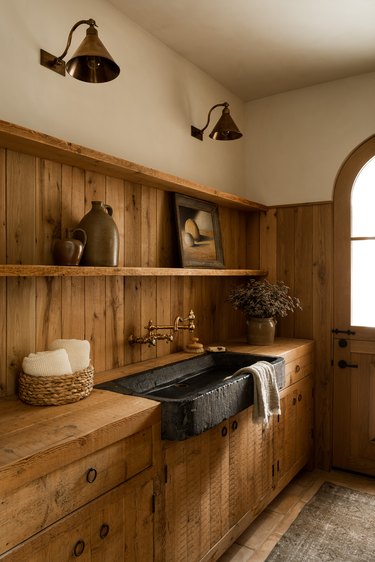 A kitchen with light wood paneling and a dark stone farmhouse sink.