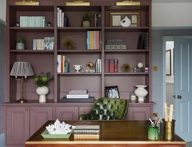 An office with a plum bookshelf, wood desk, and dark green leather chair.