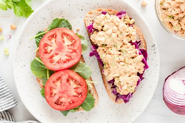 open buffalo chicken sandwich with tomatoes, lettuce, and purple cabbage