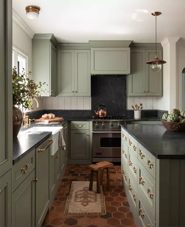 kitchen with sage green cabinets, black countertops, and gold fixtures