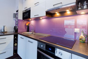 Purple glass backsplash, white cabinets, electric glass top range.