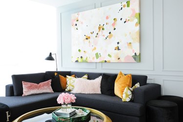Chic contemporary living room features a white wall accented with decorative moldings a showcasing a large pink and green confetti canvas art piece positioned above a charcoal gray