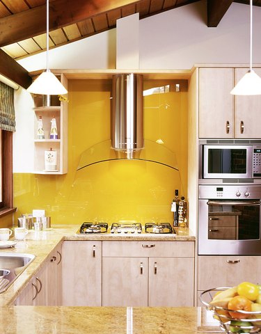 Yellow glass backsplash, light wood cabinets, glass and stainless hood.