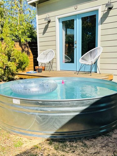 stock tank pool near home with blue door and two white chairs