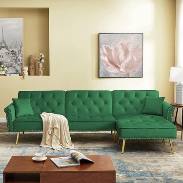 Bright green couch in yellow room with blue abstract rug. The room has a wooden coffee table and wall art