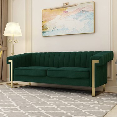 green couch with gold accents sitting in a beige room on a gray rug with a geometric pattern