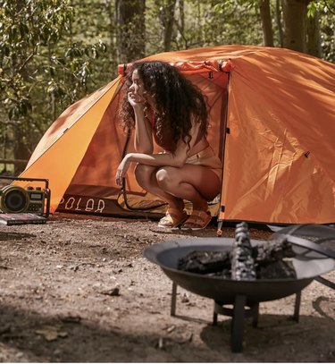 image of a female camper sitting at the entrance of her orange tent.