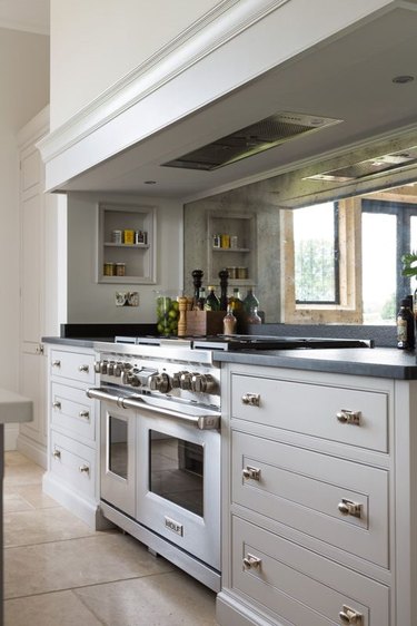 Mirrored glass backsplash, gas range, gray cabinets.