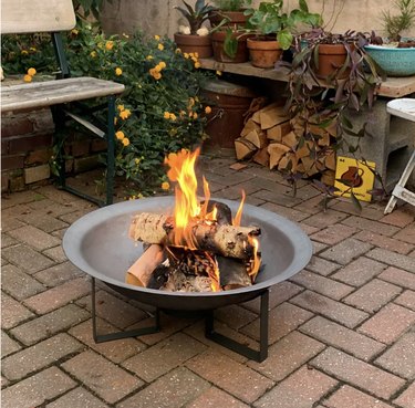 Image of a cast iron firepit with burning wood in a backyard