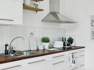 Clear glass backsplash, white cabinets, stainless hood, wood counters.