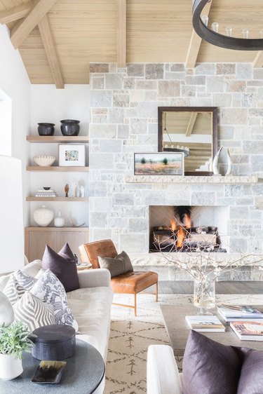 Farmhouse style living room with stone fireplace, shelves, wood ceiling.