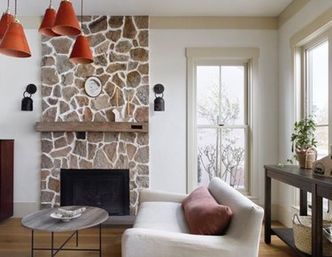 Stone fireplace with black sconces, orange pendant lamps, white couch.