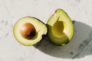 Avocado halves on a white marbled background