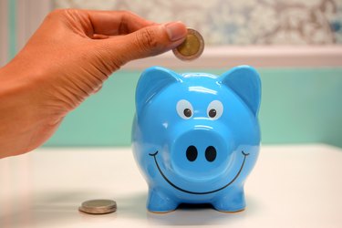 person putting coin in blue piggy bank