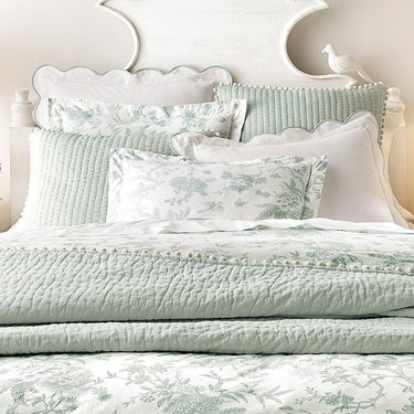 Green and white cottagecore bedding on a white bed