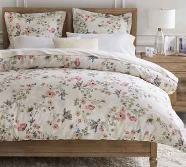 White cottagecore bedding with small colorful flowers and butterflies on a wooden bed