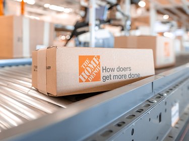 A small box with The Home Depot orange logo on a conveyor belt in a warehouse.