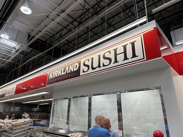 A large red, black, and white sign in a Costco warehouse that reads "Kirkland Signature Sushi"