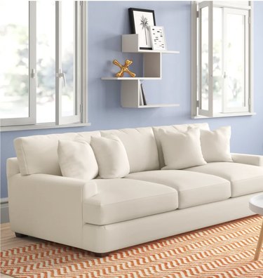 Off white couch in room with blue walls, two windows and an orange patterned rug