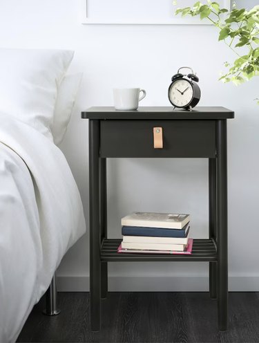 image of a black nightstand in a white room next to a bed with white linens