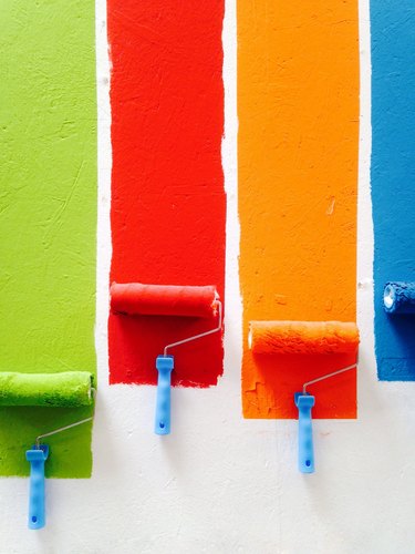 Image of paint rollers loaded with green, red, orange and blue paint rolling down a wall.