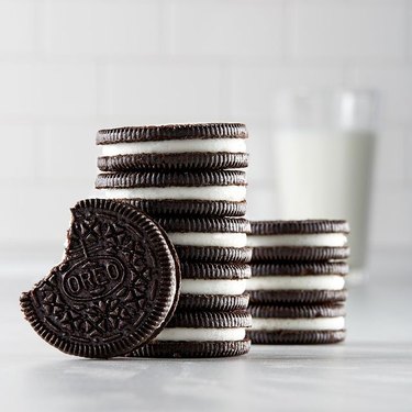 Stack of Oreos on a white countertop with a glass of milk in the background.