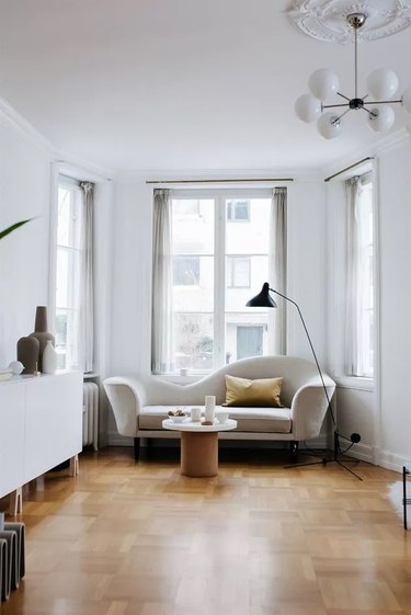 Corner of a livingroom in front of tall windows with a sofa and task lighting