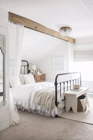 White bedroom with wooden ceiling beams and light curtains hanging from them
